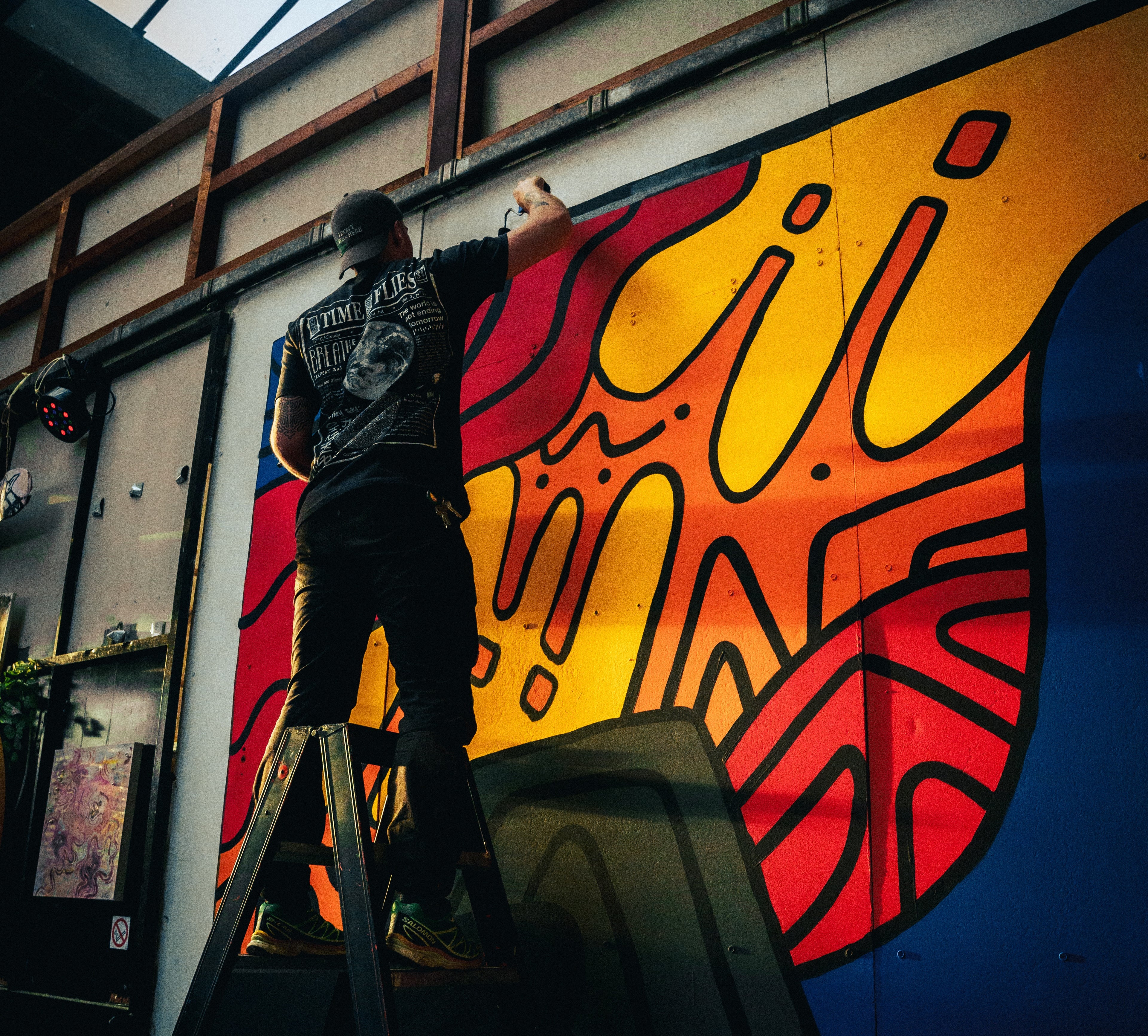 Pāku painting a colorful abstract mural on a wall.